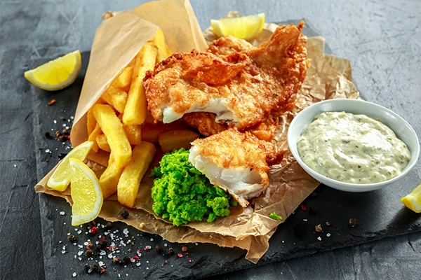 British Traditional Fish and chips with mashed peas, tartar sauce on crumpled paper.